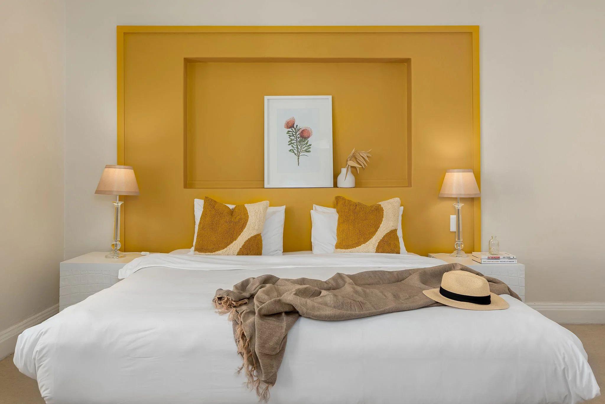 Bright Hill Suites room with bold yellow/mustard headboard niche, white bedding, and matching bedside lamps