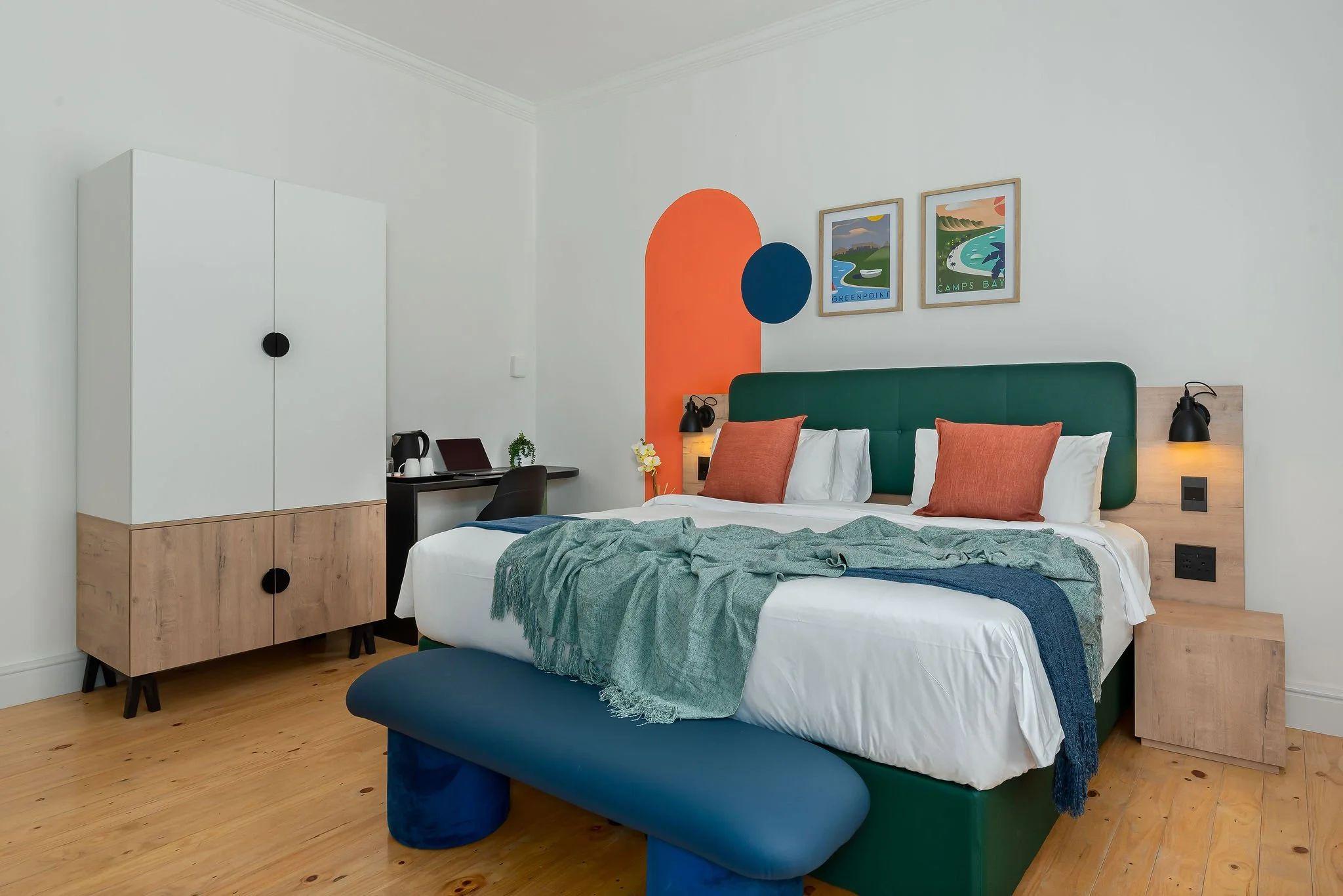 Deluxe room at Neighbourgood Hill with green upholstered headboard, colourful art prints, and orange geometric wall feature