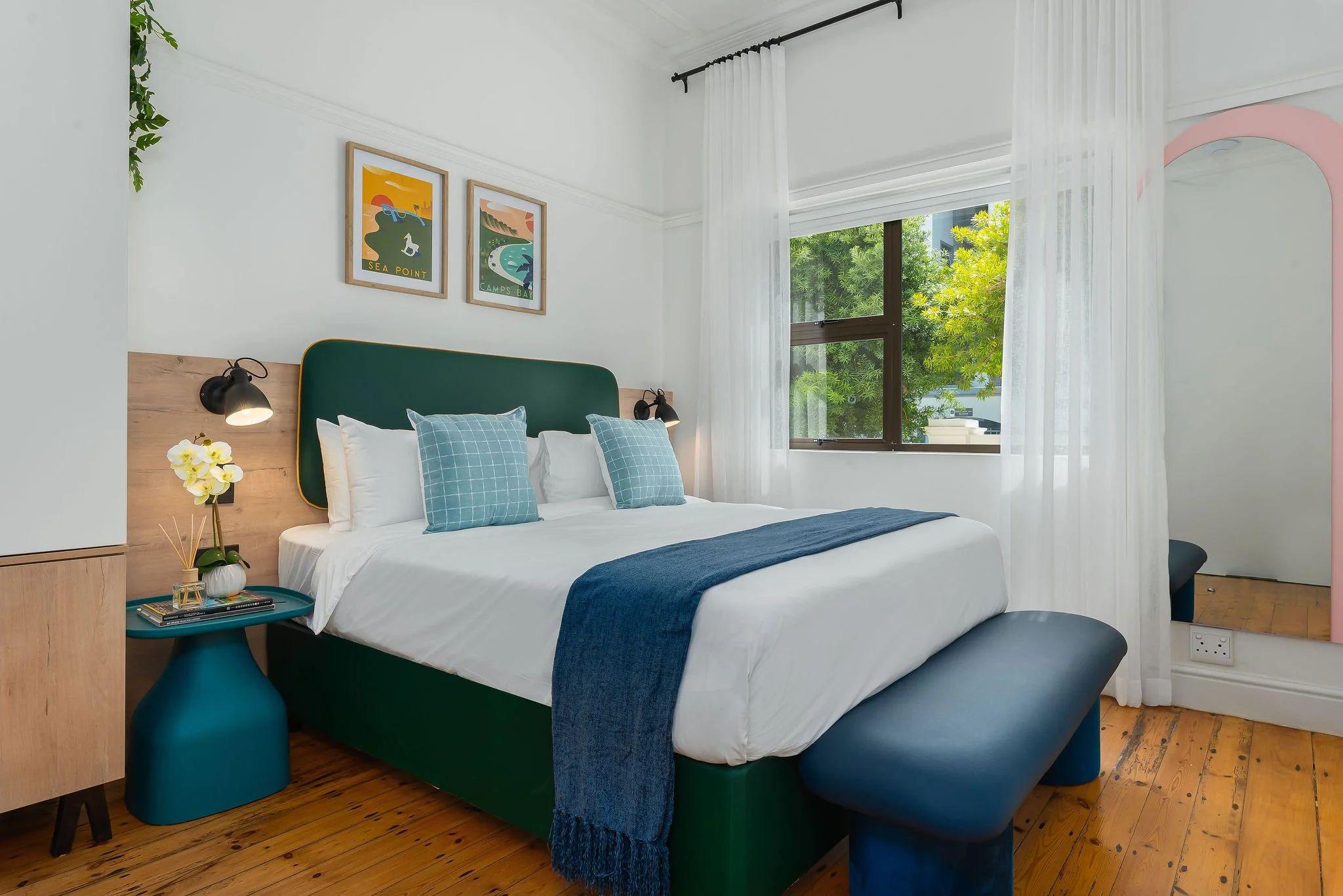 Cosy standard room at Neighbourgood Hill with green upholstered headboard, blue bench, and travel posters on the wall