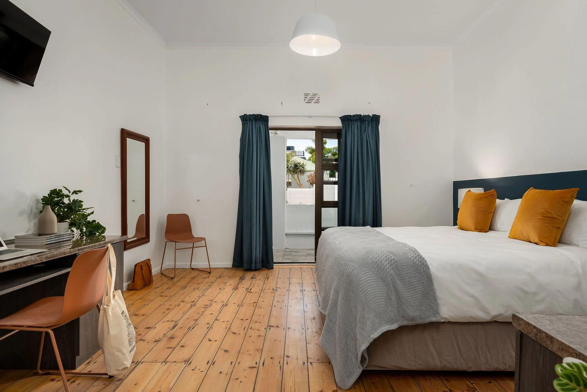 Family room with a queen-size bed, orange/yellow cushions, wooden floors, desk with chair, mirror, and blue curtains
