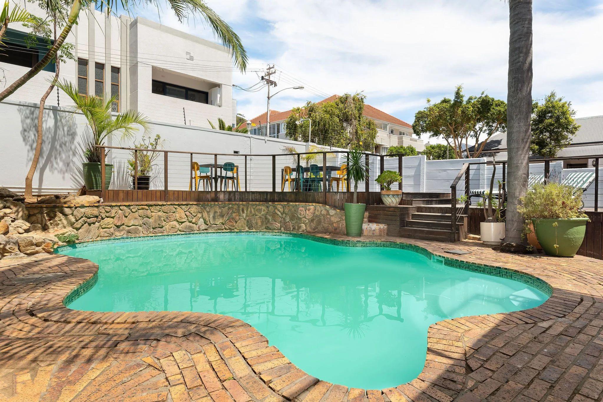 Outdoor swimming pool with brick surround, palm trees, and the rooftop deck with colourful chairs visible above
