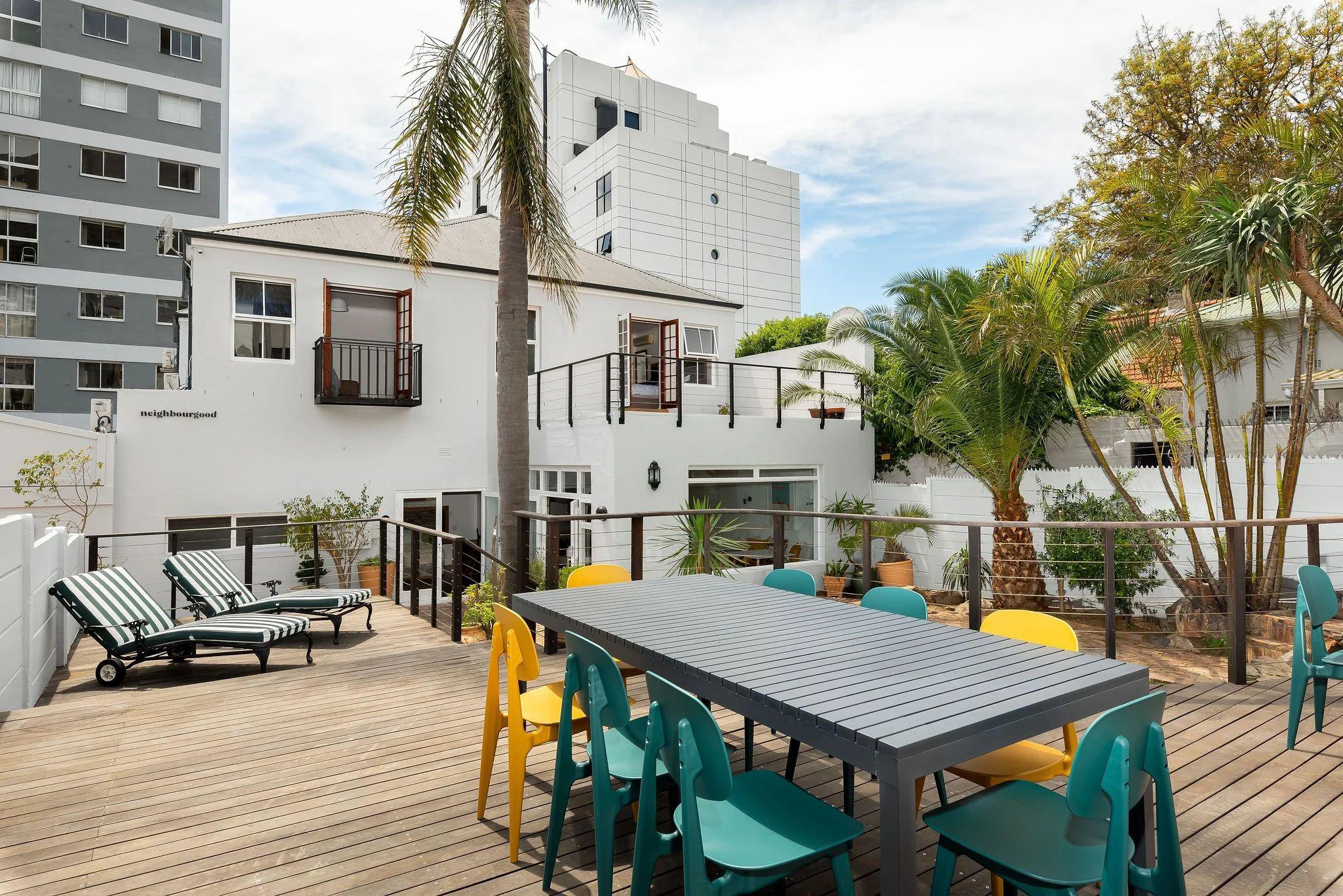 Outdoor rooftop deck with a large dining table, colourful chairs, sun loungers, and a view of the pool and surrounding Green Point neighbourhood