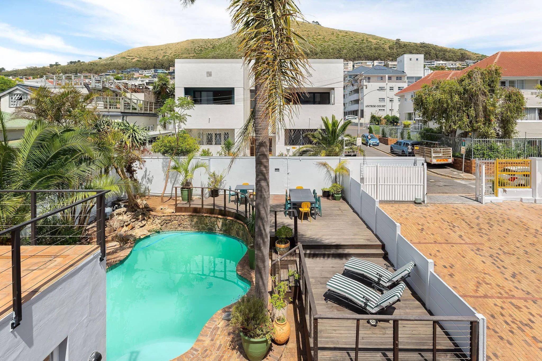 Aerial view of the outdoor pool, sun deck with loungers, and surrounding Green Point neighbourhood with Signal Hill in the background