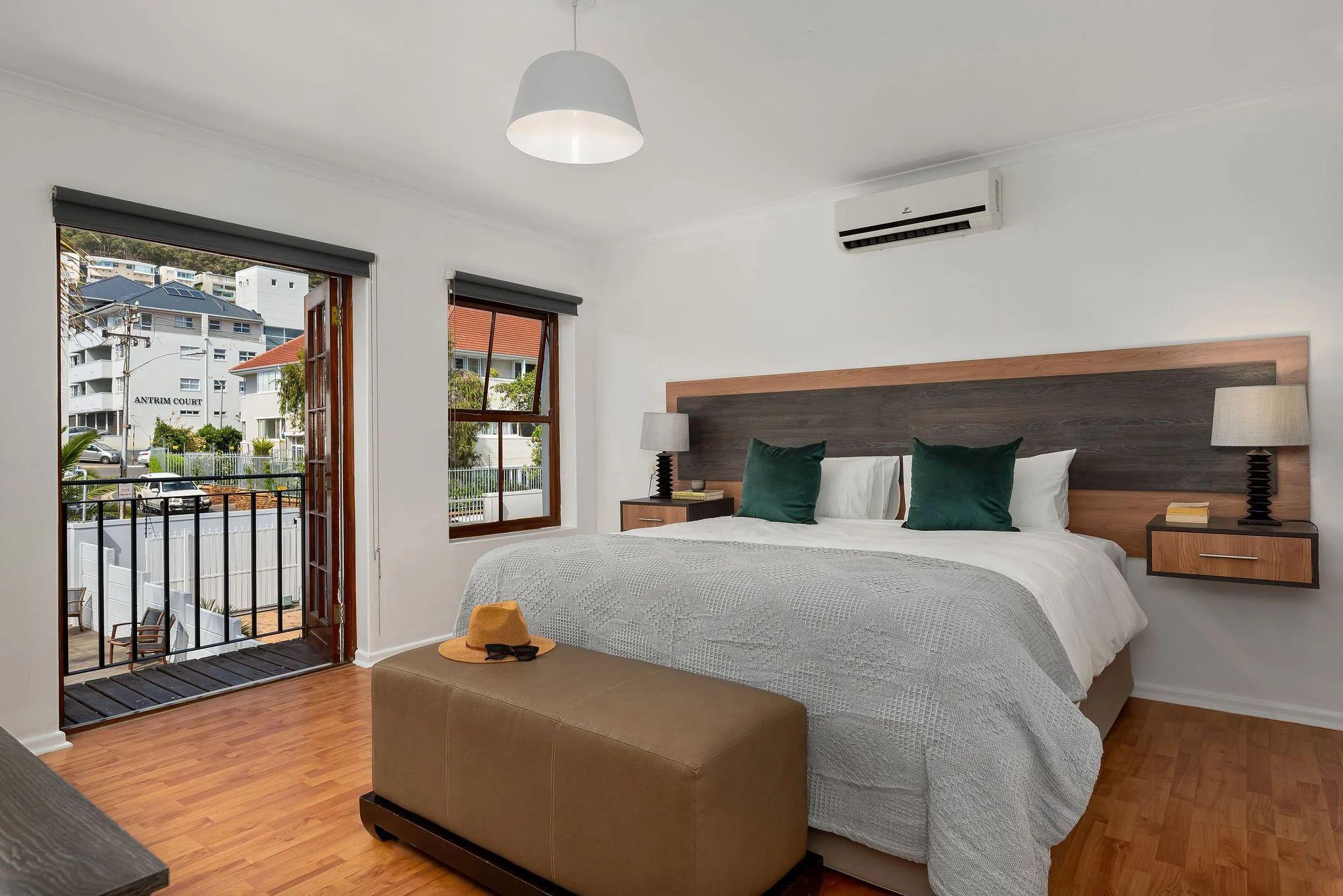 Superior room with a king-size bed, green cushions, open balcony door with street view, air conditioning unit, and wooden floors