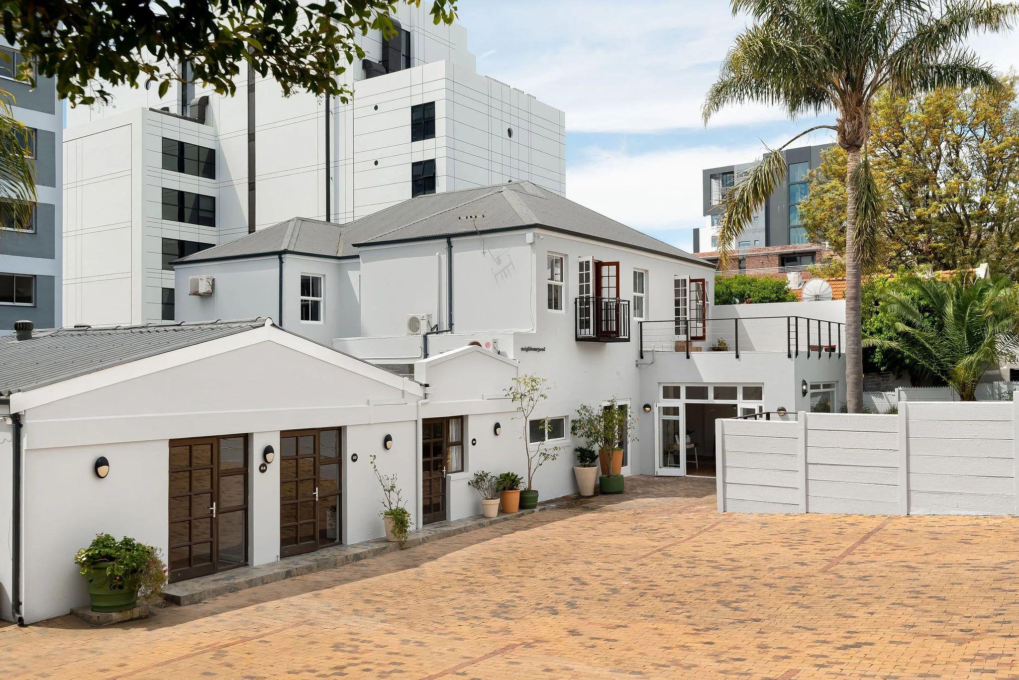 Exterior view of the Ravenscraig property showing the white heritage building with wooden doors, courtyard, and palm trees