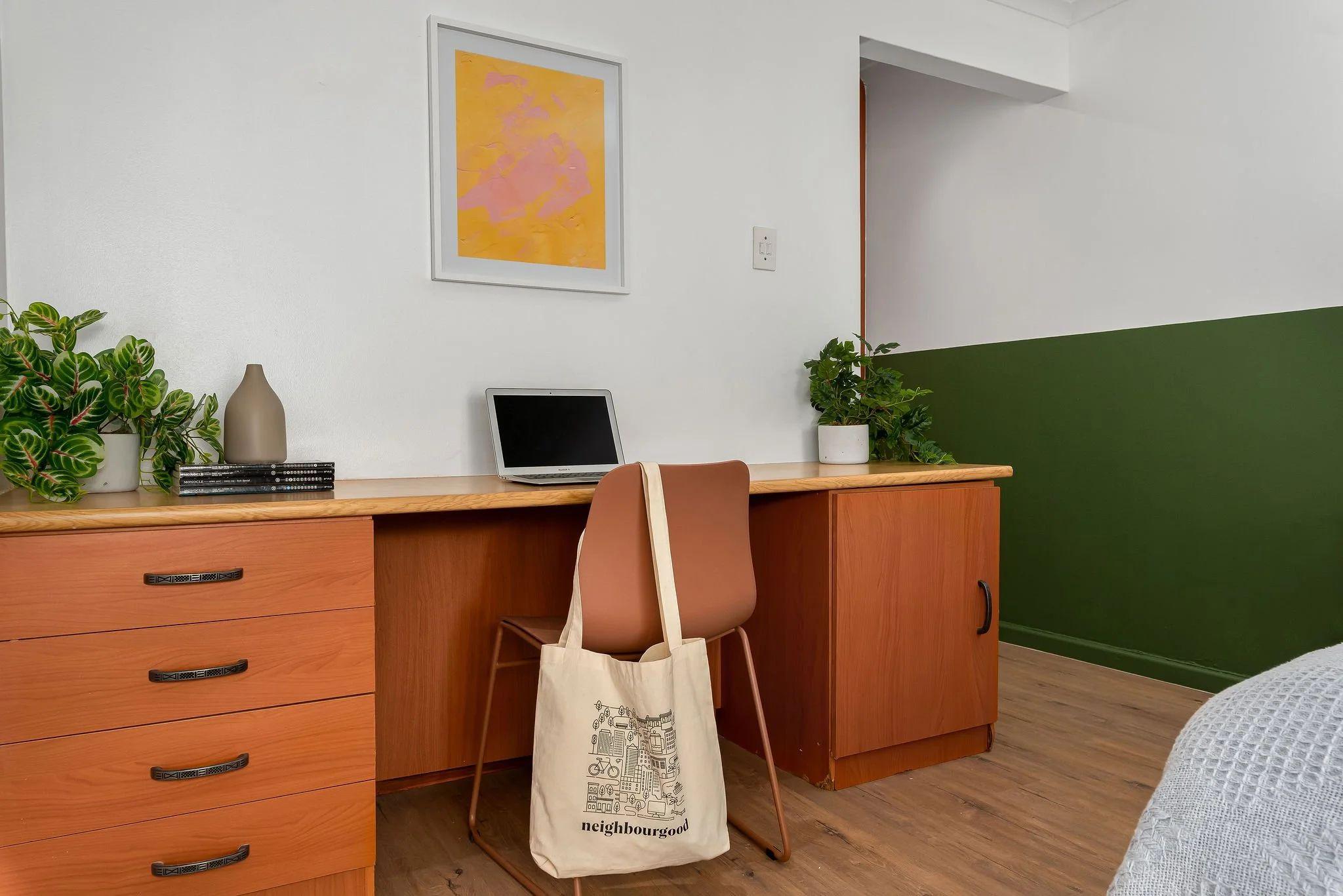 In-room desk area with a wooden desk, laptop, chair, and green accent wall — part of a deluxe room