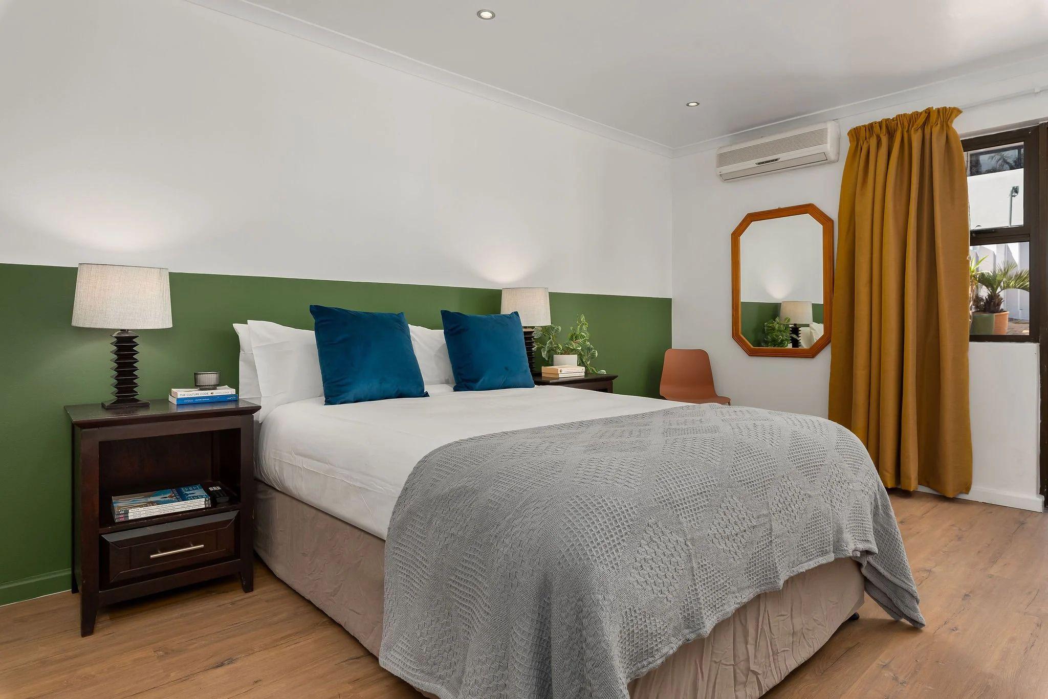 Superior room with a queen-size bed, blue cushions, green accent wall, mustard curtains, octagonal mirror, and air conditioning