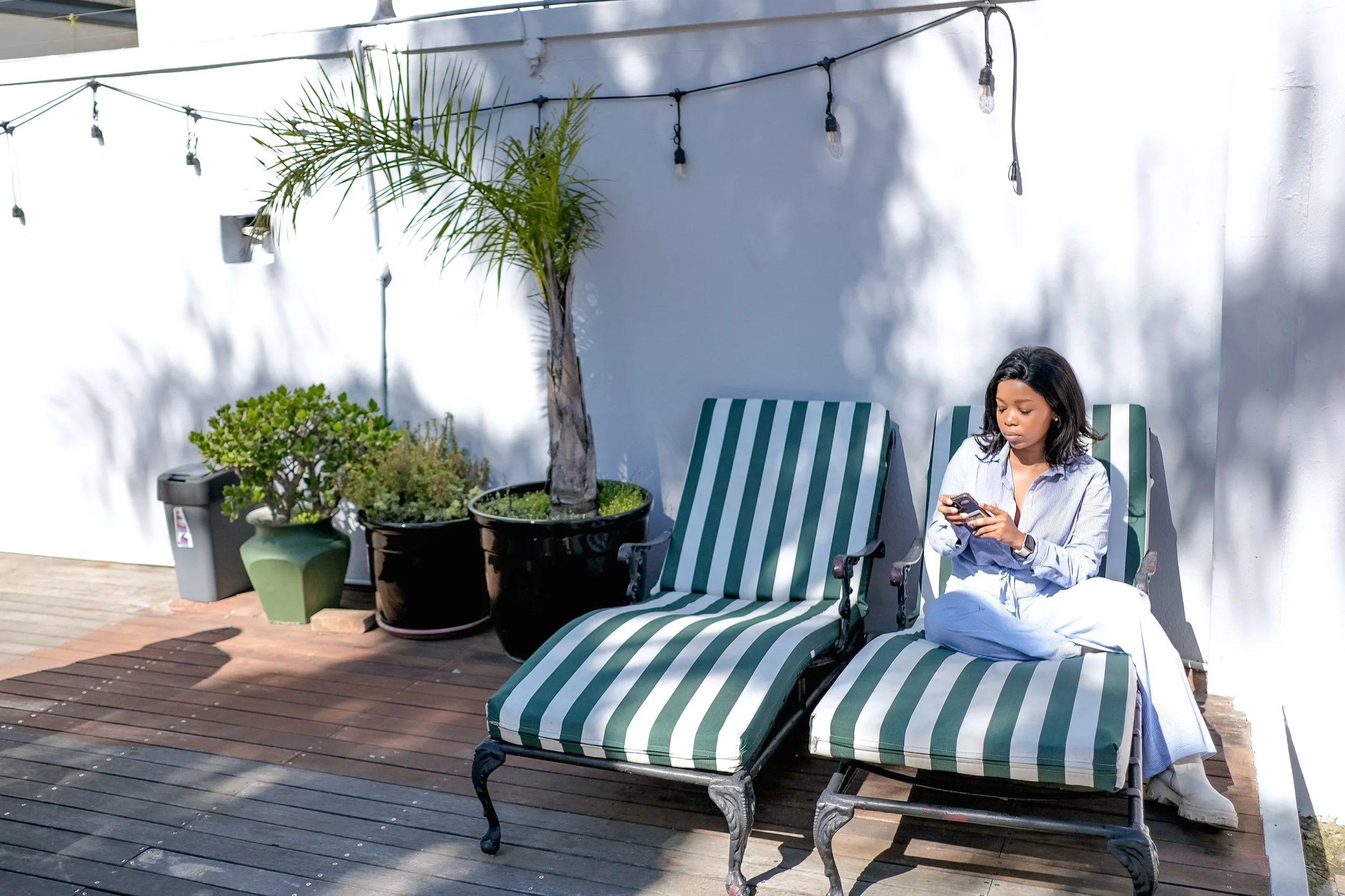 Guest relaxing on a striped sun lounger on the outdoor deck area with potted plants and string lights