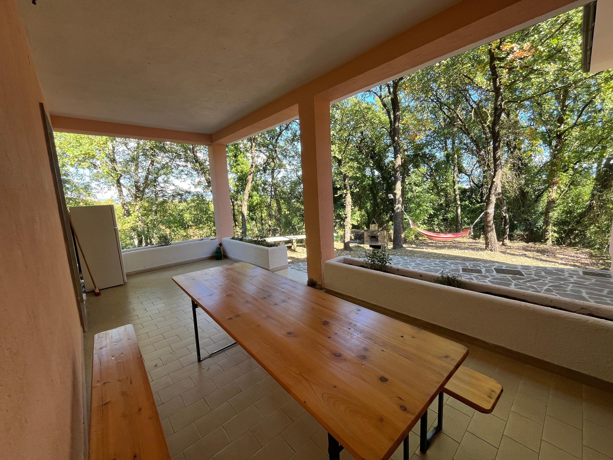 Back veranda with wooden table and bench, overlooking the garden with hammock and trees