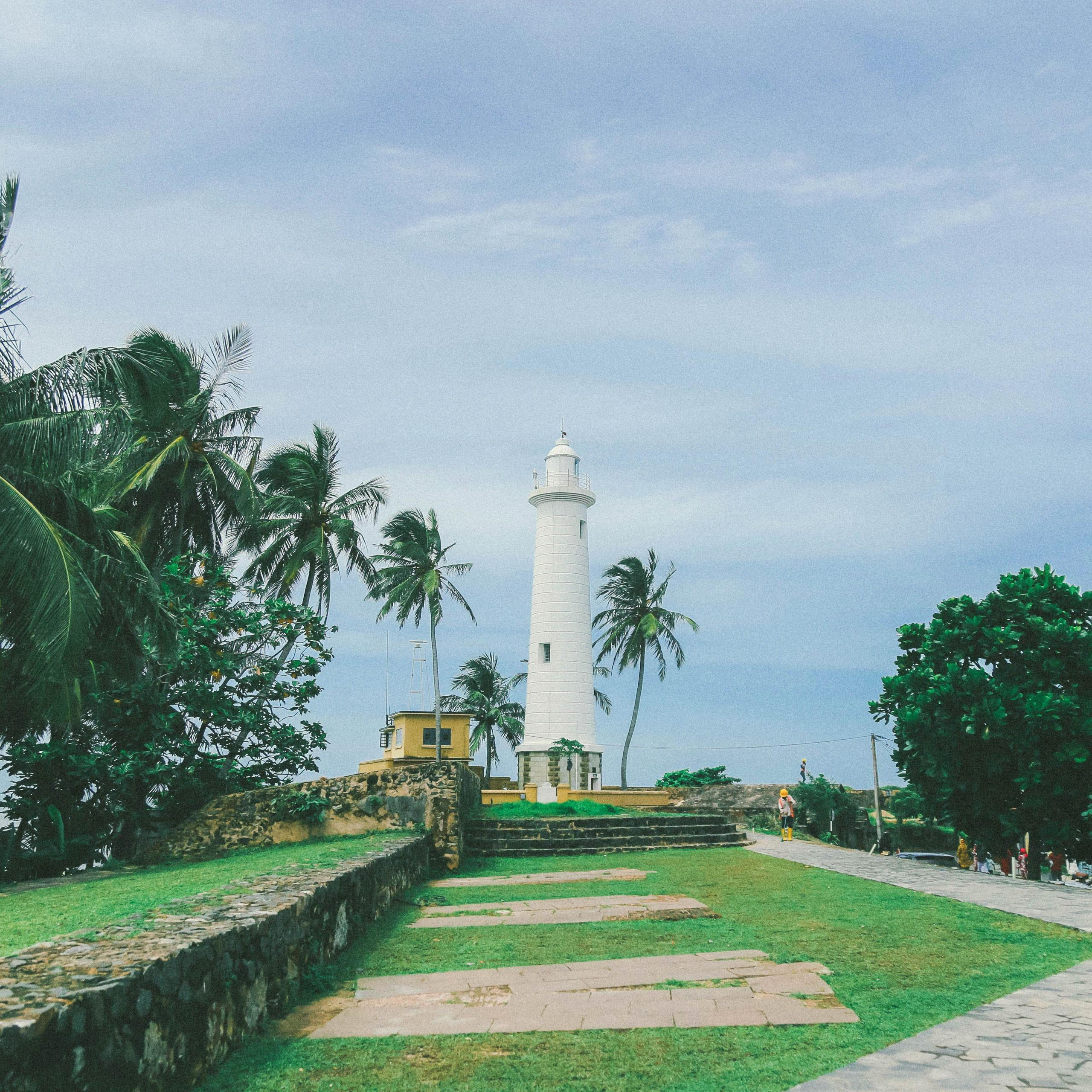 The historic lighthouse at Galle Fort, standing tall against a backdrop of clear skies and ocean.