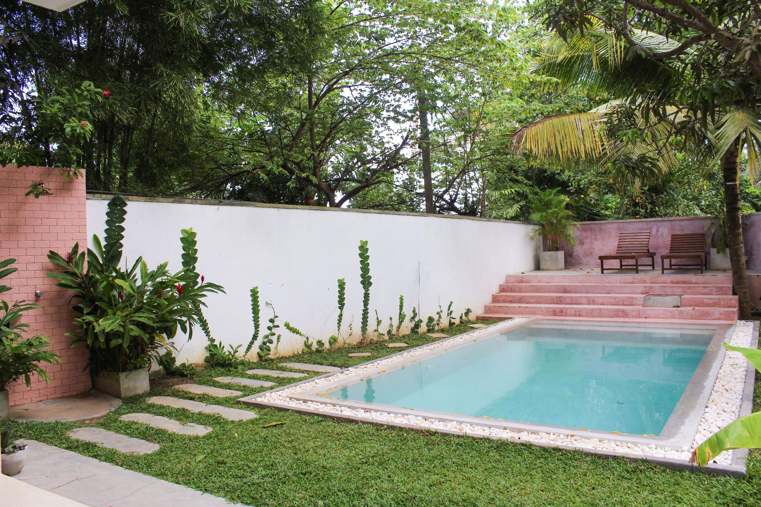 Swimming pool and adjacent shower area at NETS Cowork and Colive, surrounded by tropical plants and modern design elements.