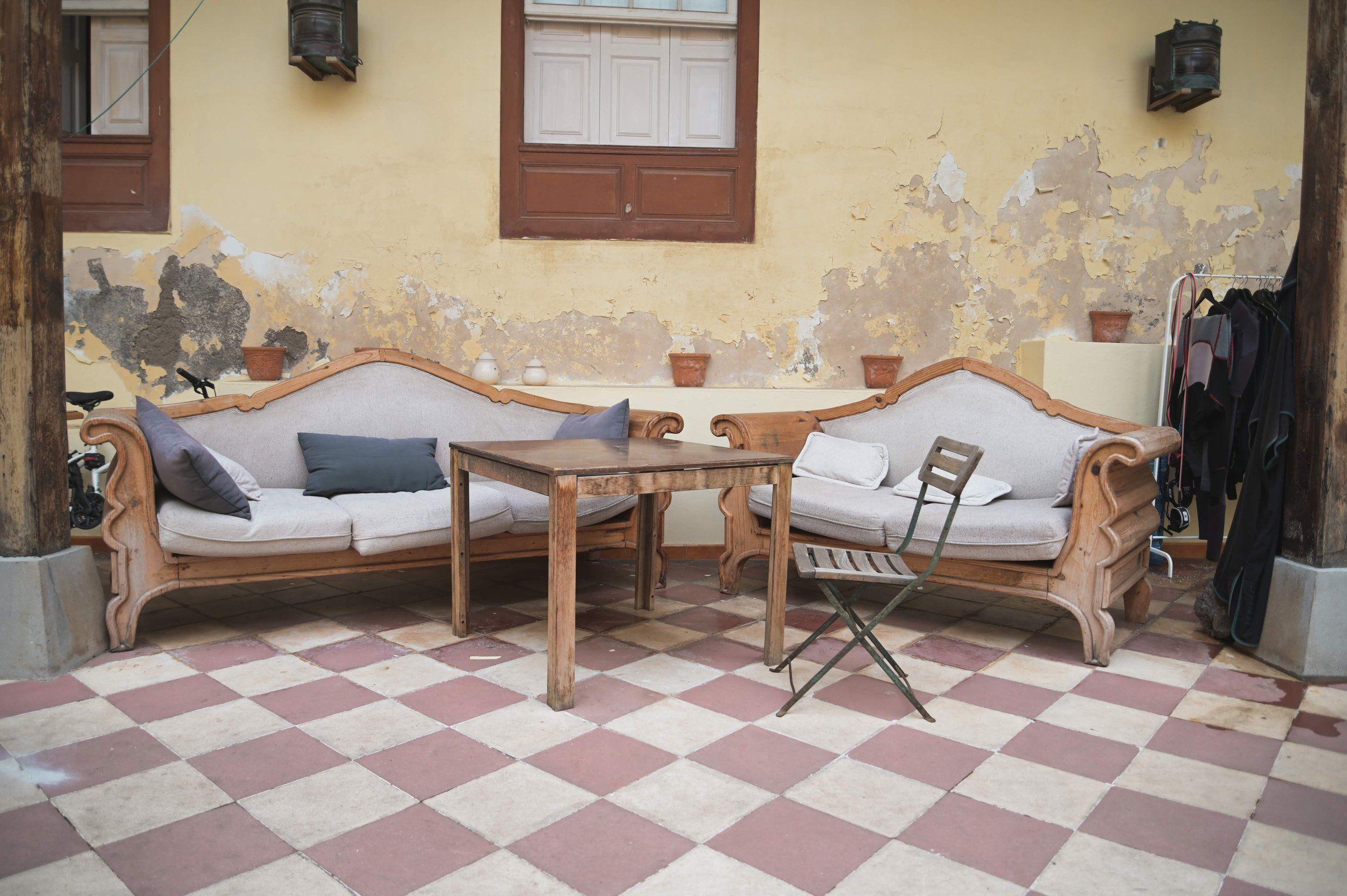 The internal patio of Nine Coliving featuring two ornate vintage wooden sofas with cushions, a small table, and a checkered tile floor against a rustic yellow wall.