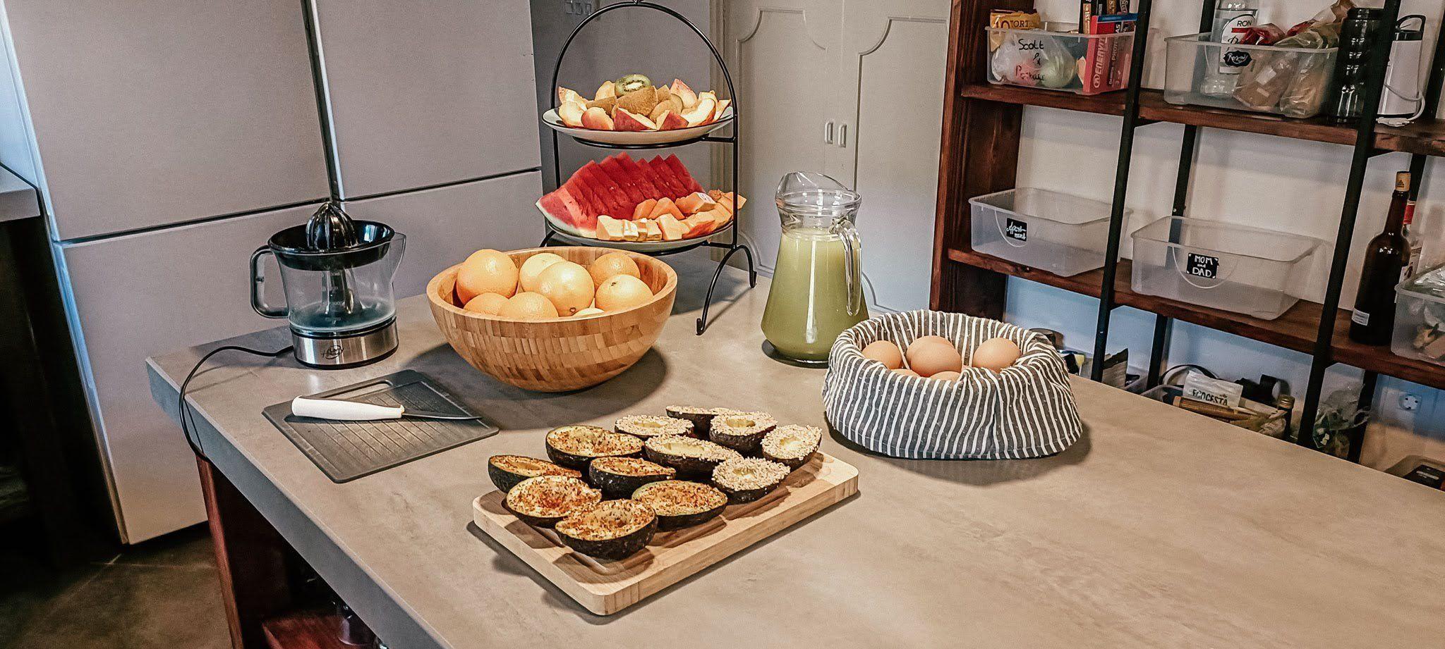Breakfast preparation on the kitchen counter with avocados, fruits, and fresh juice.