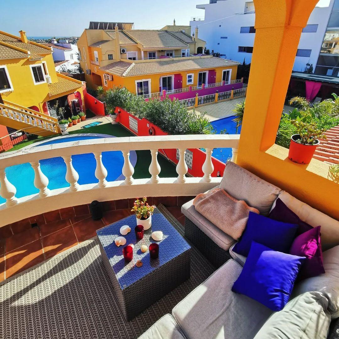 Balcony with lounge seating overlooking the swimming pools and colorful villas of Noma Village