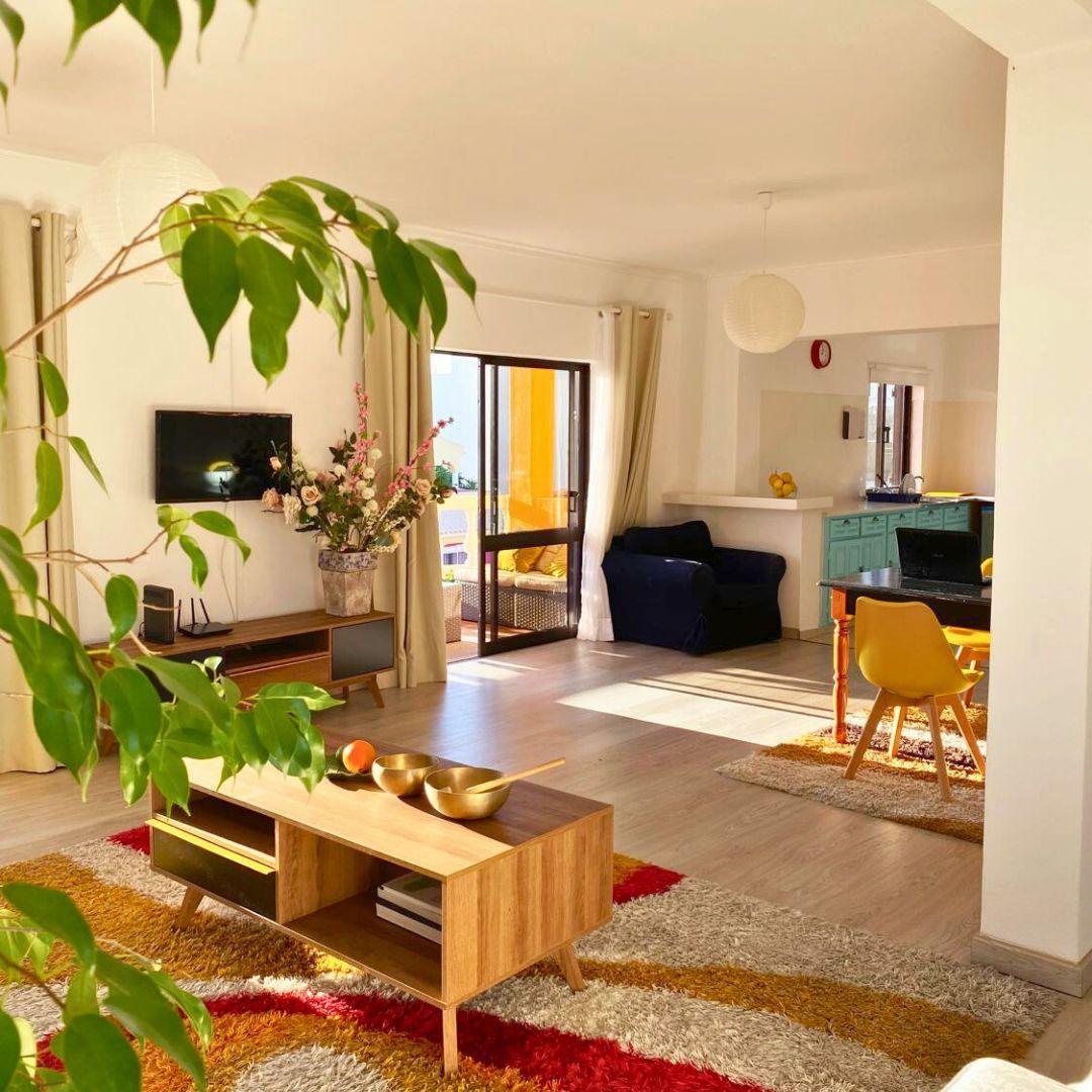 Open-plan lounge and living area inside the coliving house with plants, sofa, TV and kitchen visible