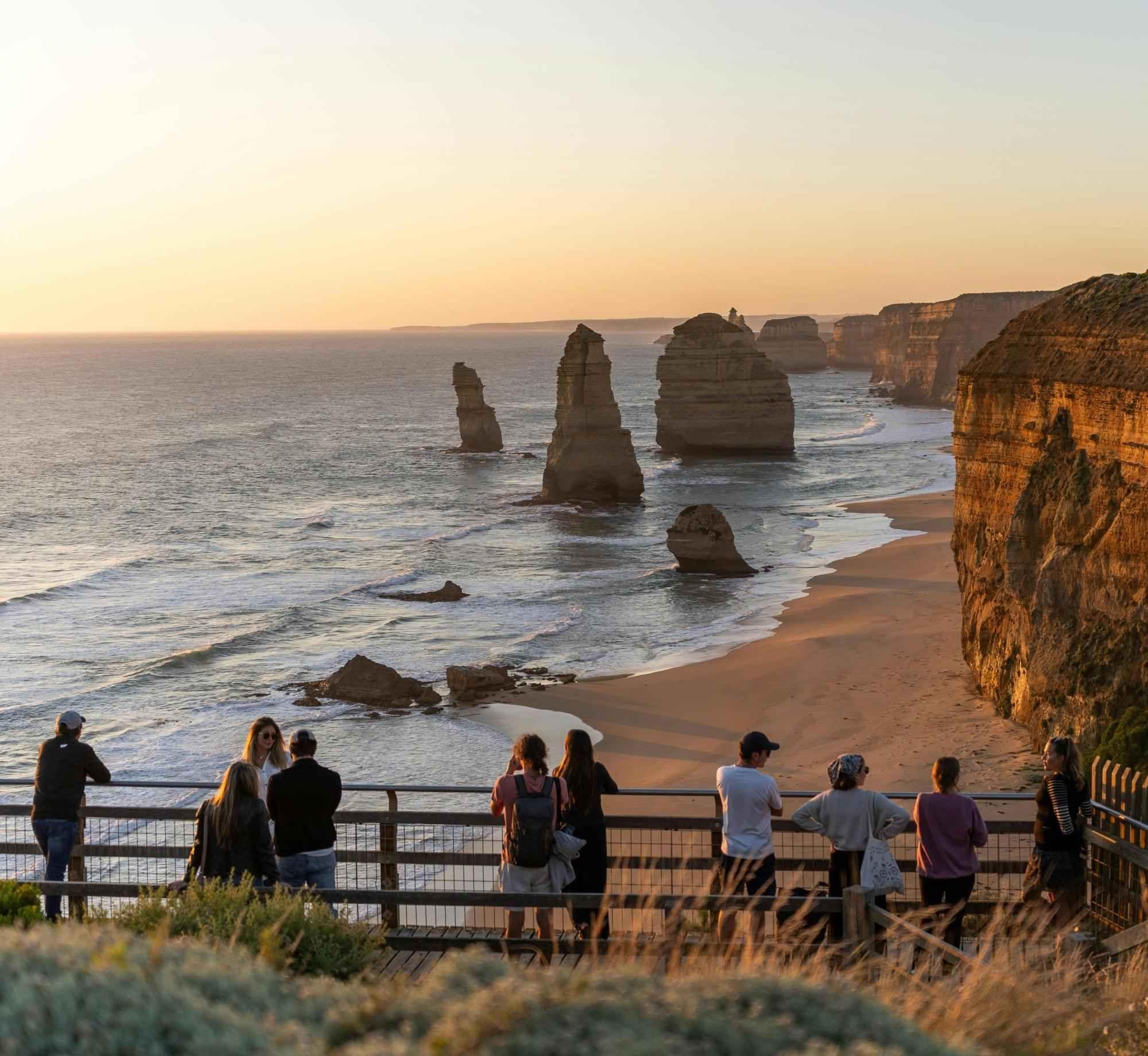 Group of people standing at a viewpoint overlooking dramatic coastal cliffs and ocean at sunset