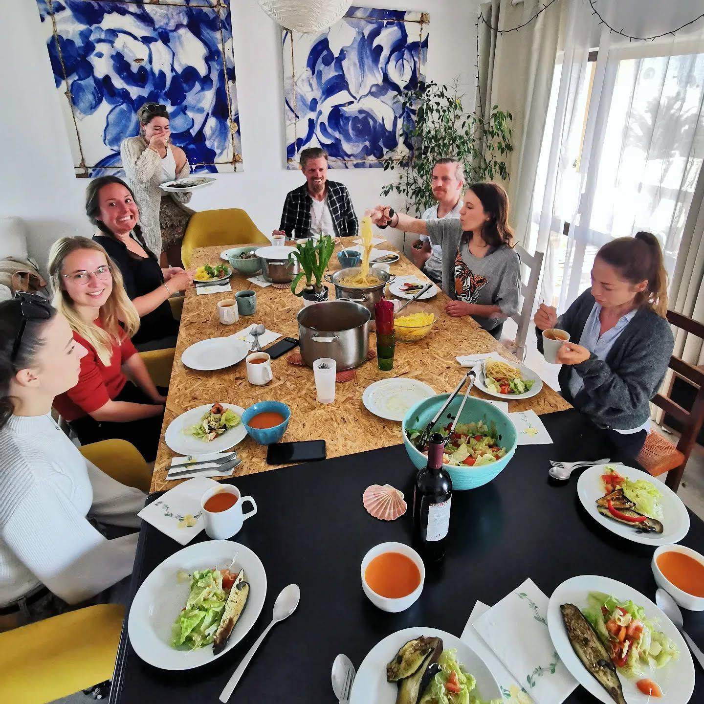Community dinner — group of members sharing a meal around a large table with blue artwork on the walls