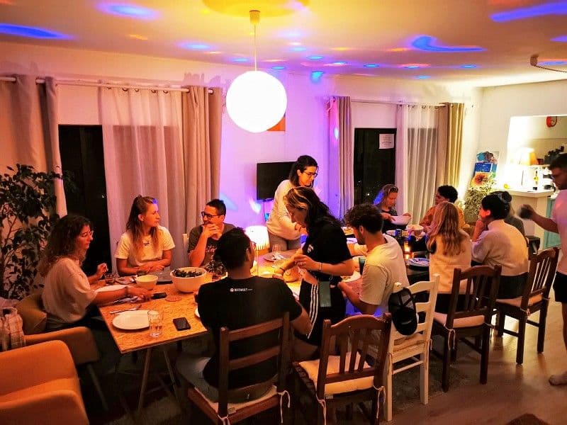 Group dinner in the common area at Noma Village — community members gathered around a table with colorful lighting