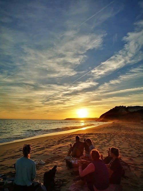 Community members sitting on the beach at sunset in Lagos, Portugal