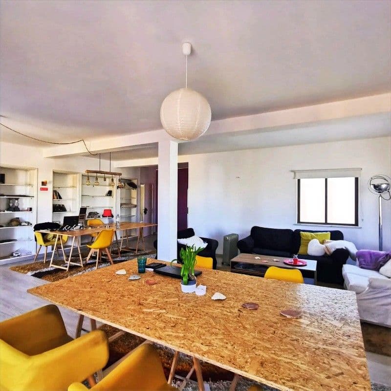 Professional coworking space with 500 Mbps high-speed WiFi for digital nomads in Lagos Portugal — open-plan with large wooden desk, yellow chairs, lounge area and balcony access