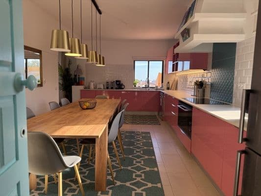 Fully equipped shared kitchen in coliving space — pink/rose cabinetry with dining table and pendant lights