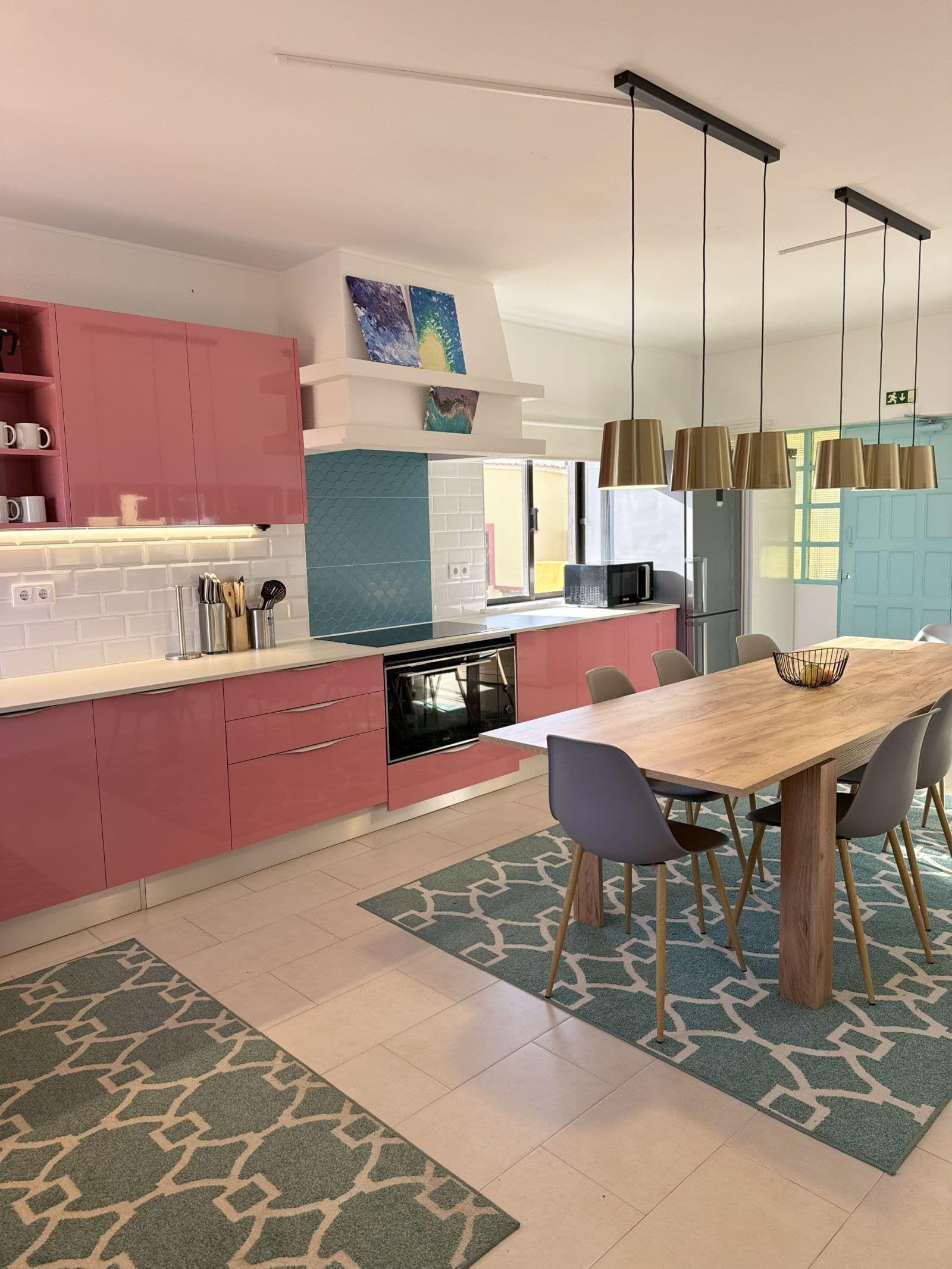 Communal kitchen with pink cabinetry, dining table and pendant lights