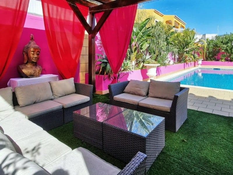 Swimming pool and outdoor coworking areas at Noma Village coliving Lagos Portugal — poolside lounge with rattan furniture and pink walls