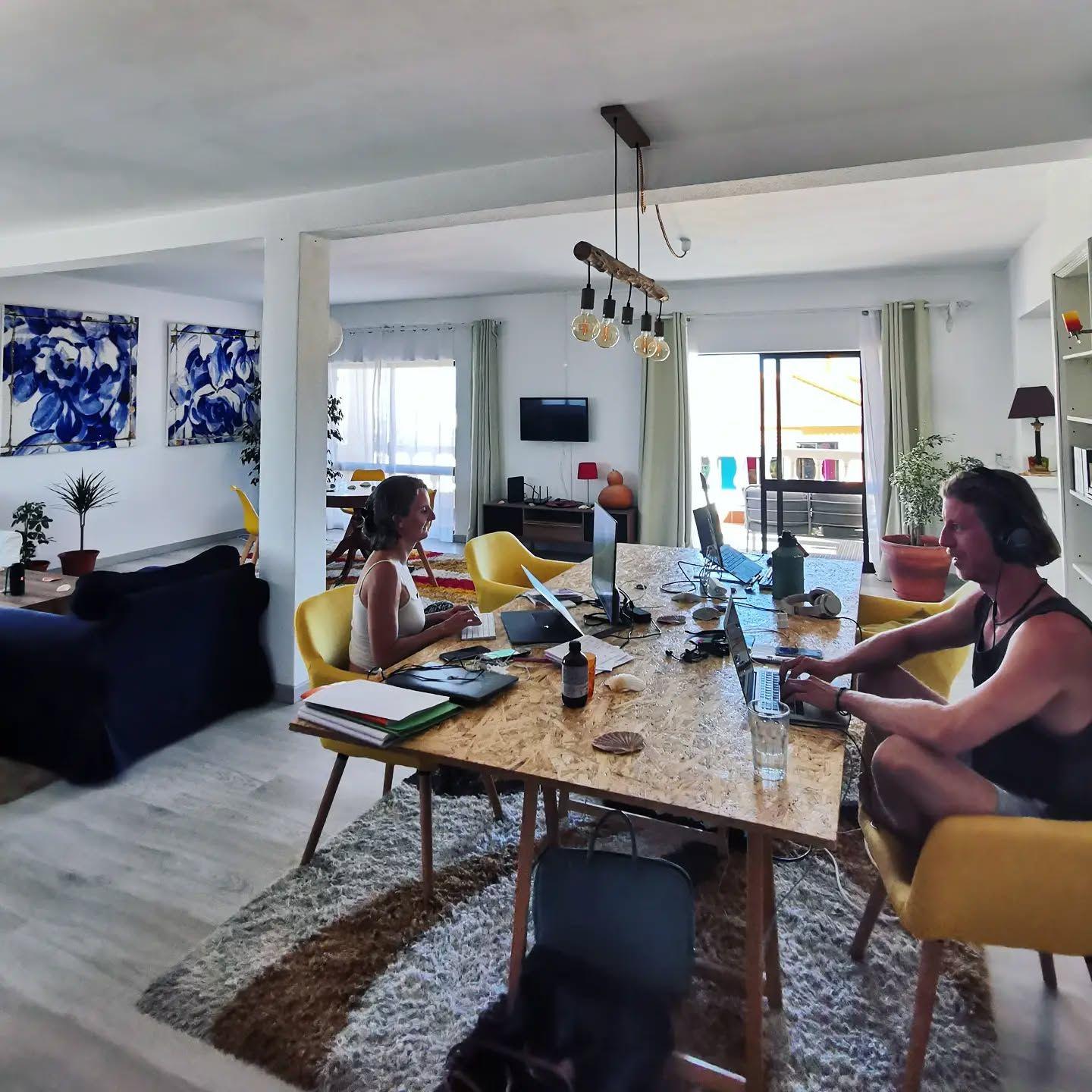 Cowork space — two people working on laptops at a large wooden desk in the open-plan coworking area