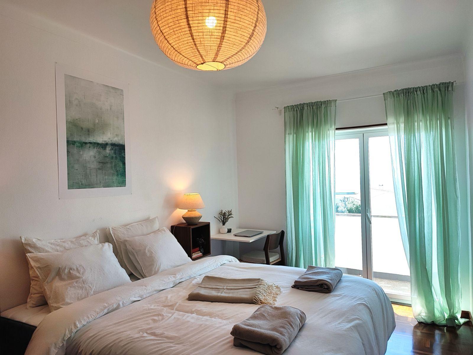 Bright private bedroom with double bed, desk and green curtains at Laura's Home coliving