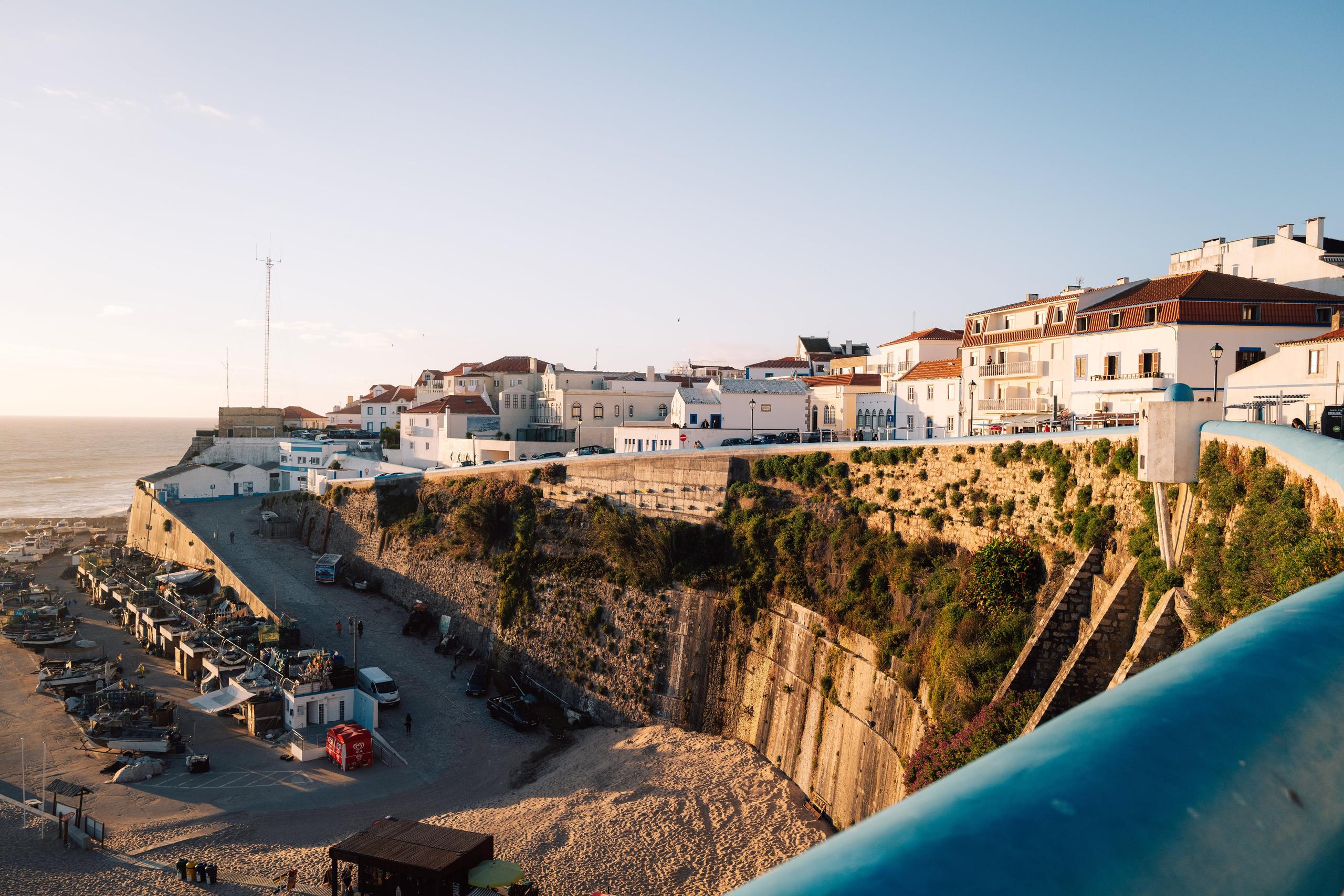 Panoramic view of Ericeira's coastal village with white buildings on cliffs above the ocean at sunset