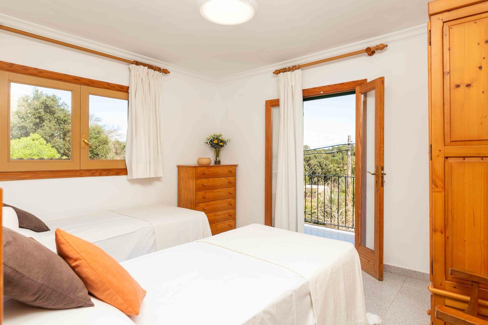 A bright private twin room with two beds, wooden furniture, and a balcony door