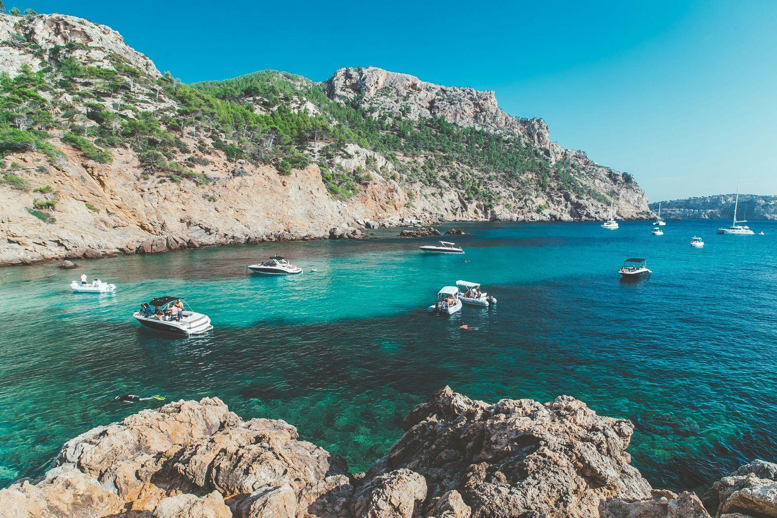 Boats anchored in a turquoise cove surrounded by rocky cliffs in Mallorca