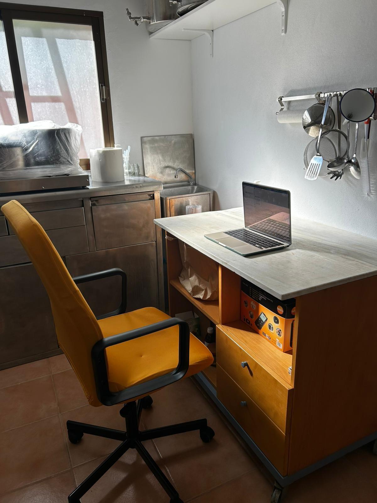 A desk with laptop and office chair set up in the coworking kitchen area