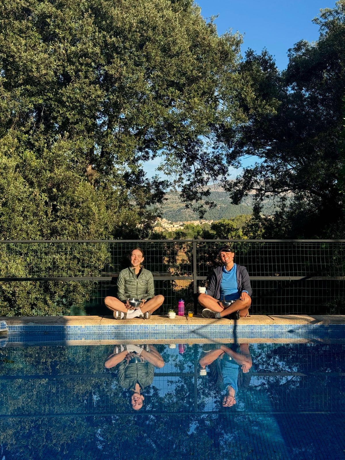 Two guests sitting by the pool with mountain views in the background