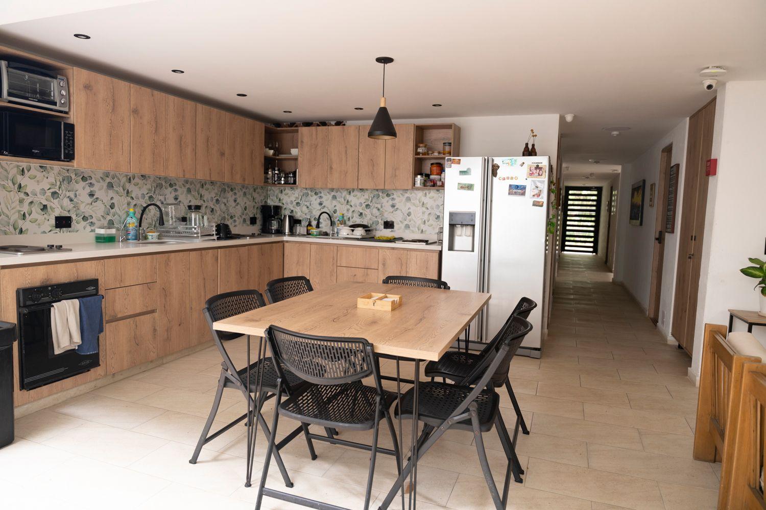 Fully equipped shared kitchen with wooden cabinets, dining table, and refrigerator