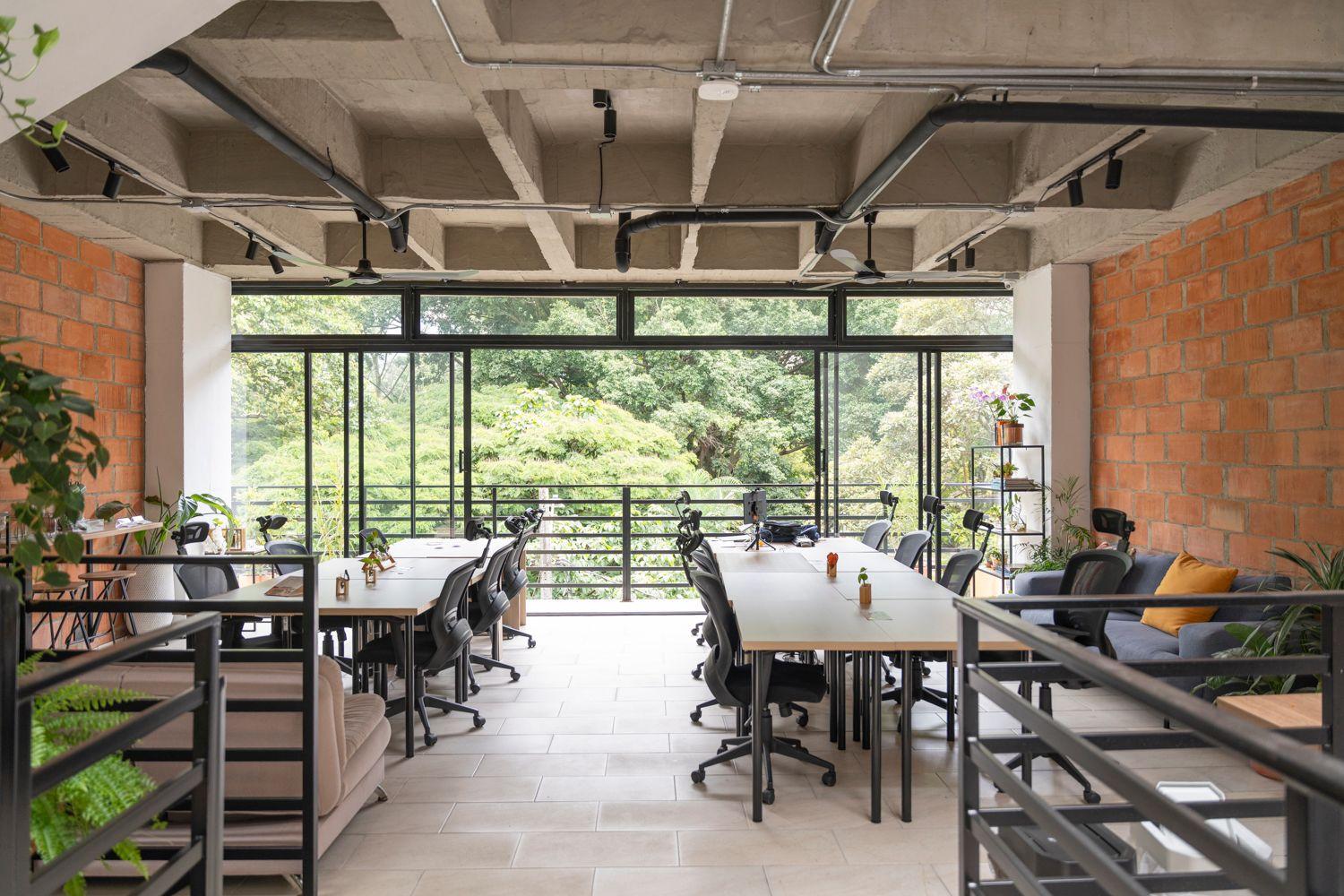 Newly renovated coworking floor with ergonomic chairs, long desks, brick walls, and floor-to-ceiling windows overlooking lush park