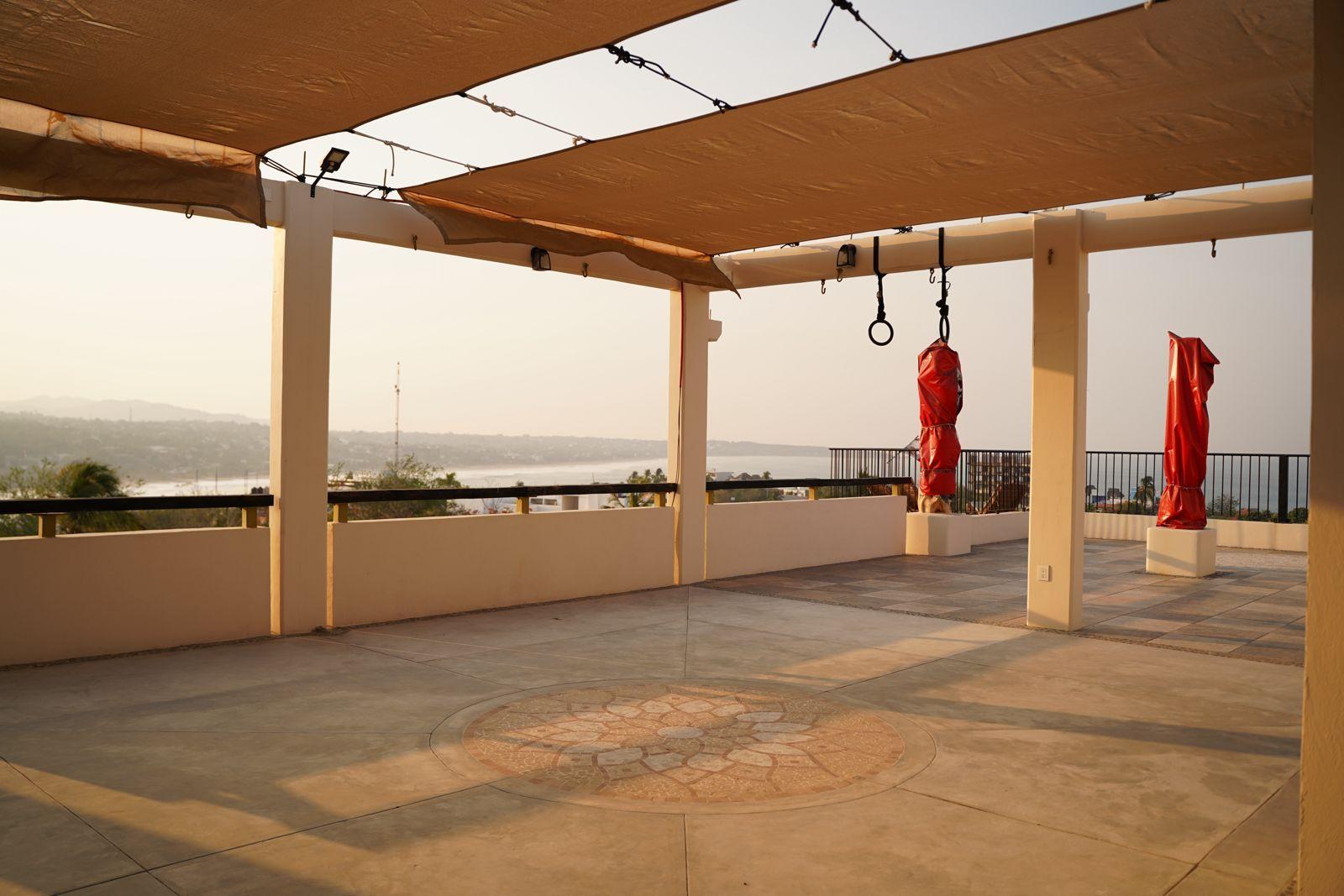 Rooftop gym and yoga space with shaded canopy, punching bags, gymnastic rings, and ocean views