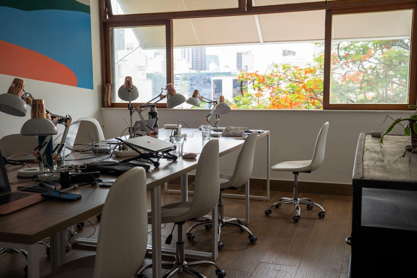 Bright dedicated coworking room with a large table, individual desk lamps, white chairs, and large windows overlooking a blossoming tree