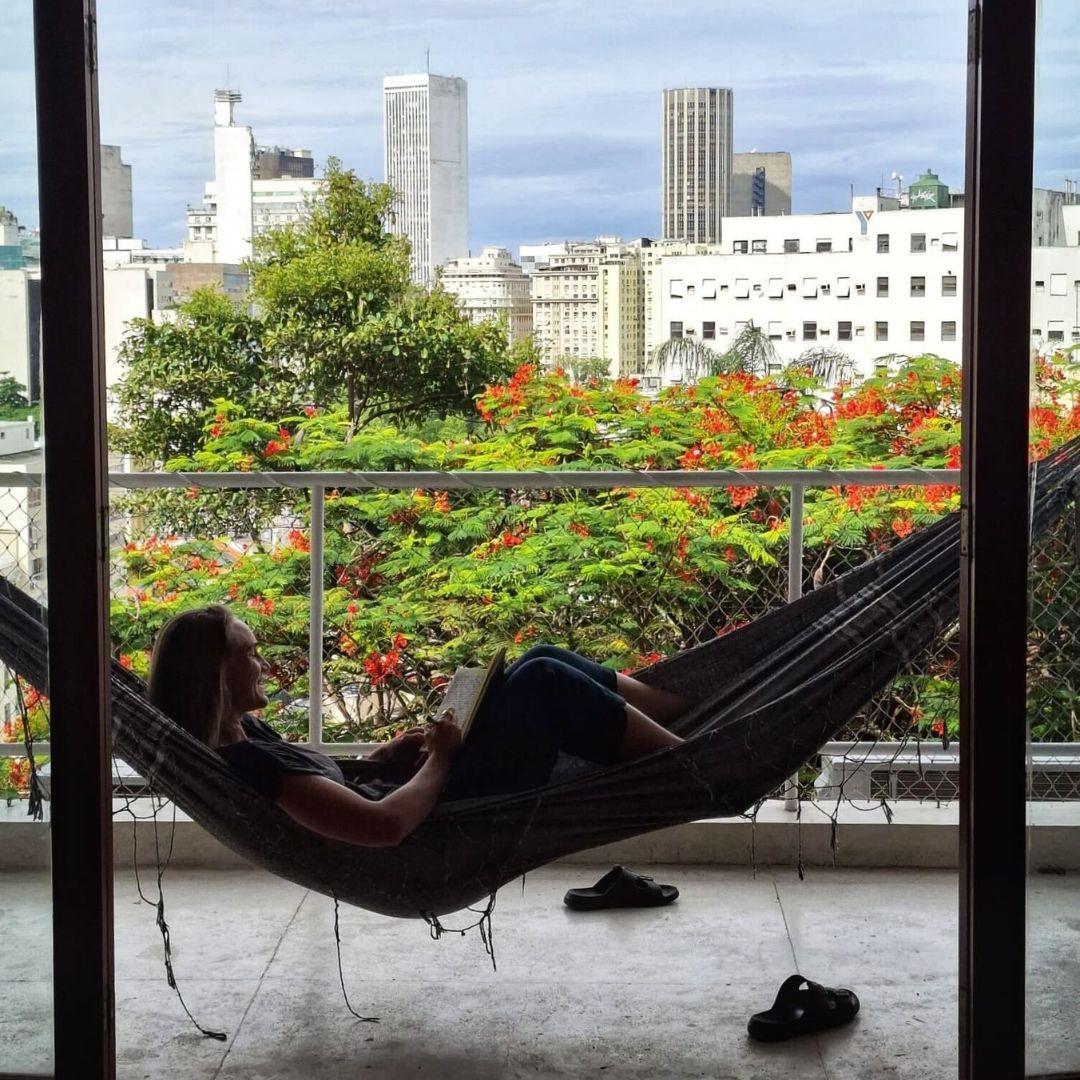 A person relaxing in a hammock on the coworking balcony, reading a book with a view of the city skyline and flowering trees