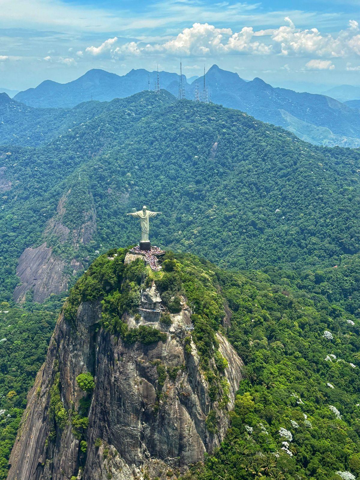 Aerial view of Christ the Redeemer statue atop Corcovado mountain surrounded by lush green rainforest
