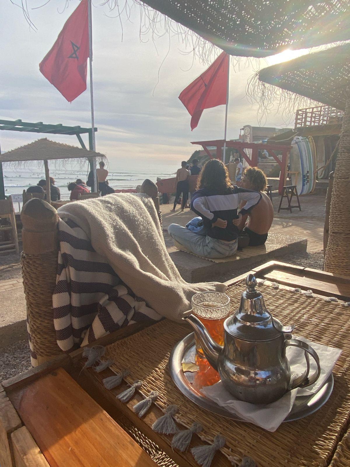 Traditional Moroccan mint tea served at a beachfront café in Taghazout with surfers in the background