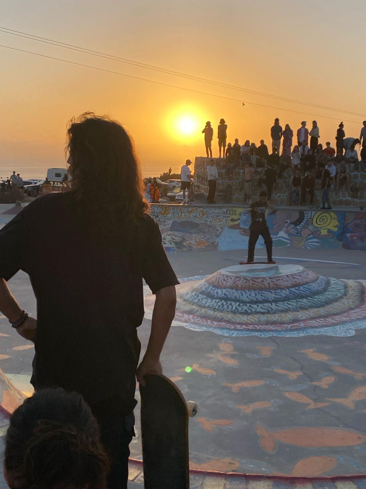 Skateboarders and crowd at the Taghazout skate park during golden hour sunset