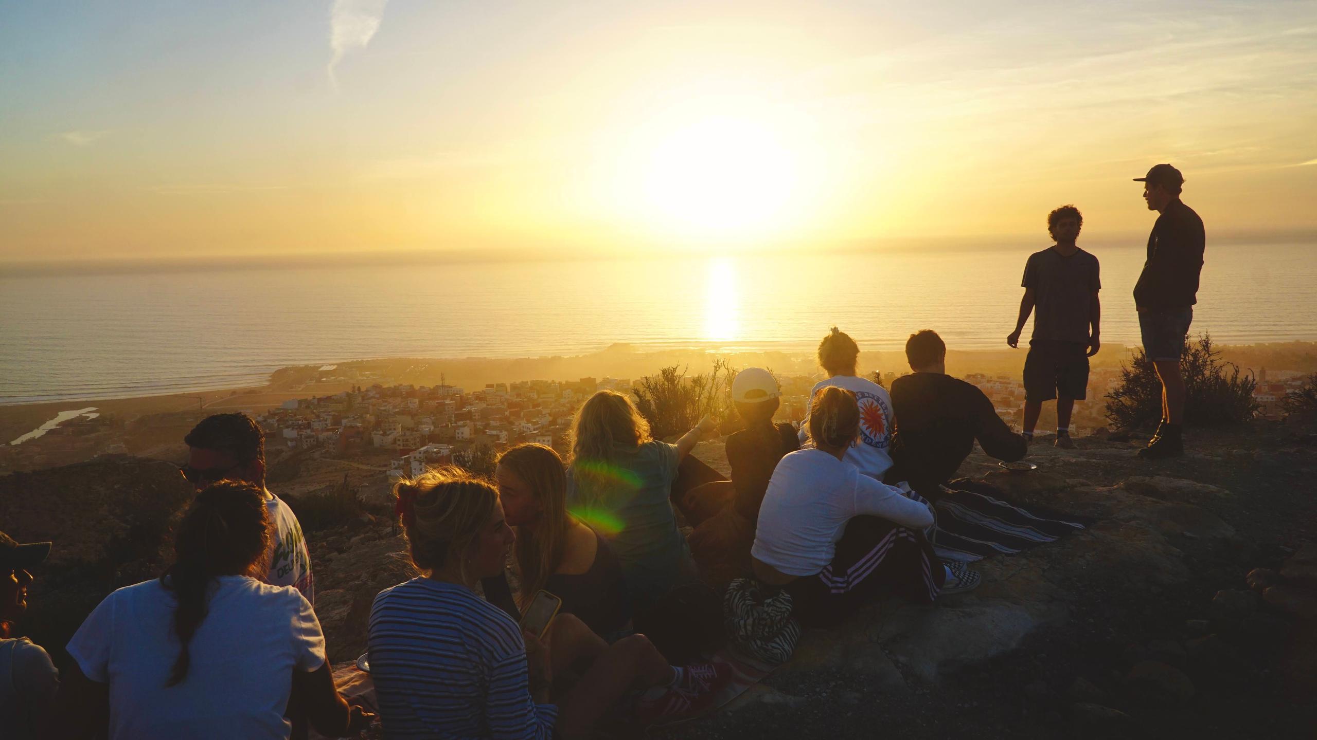 Group of people watching the sunset over the ocean from a hilltop near Taghazout Bay