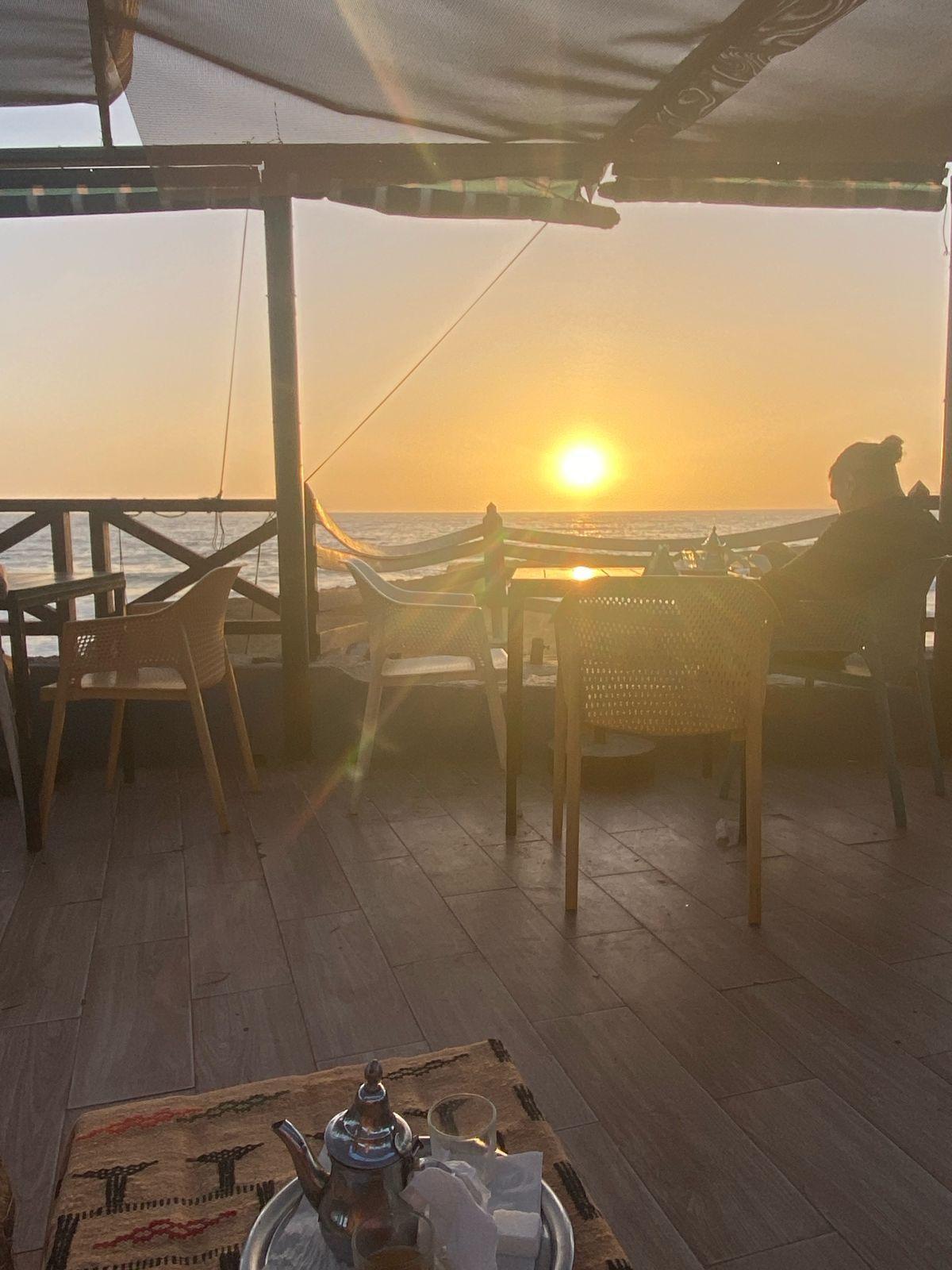 Café terrace with wicker chairs overlooking the ocean at sunset near Tamraght