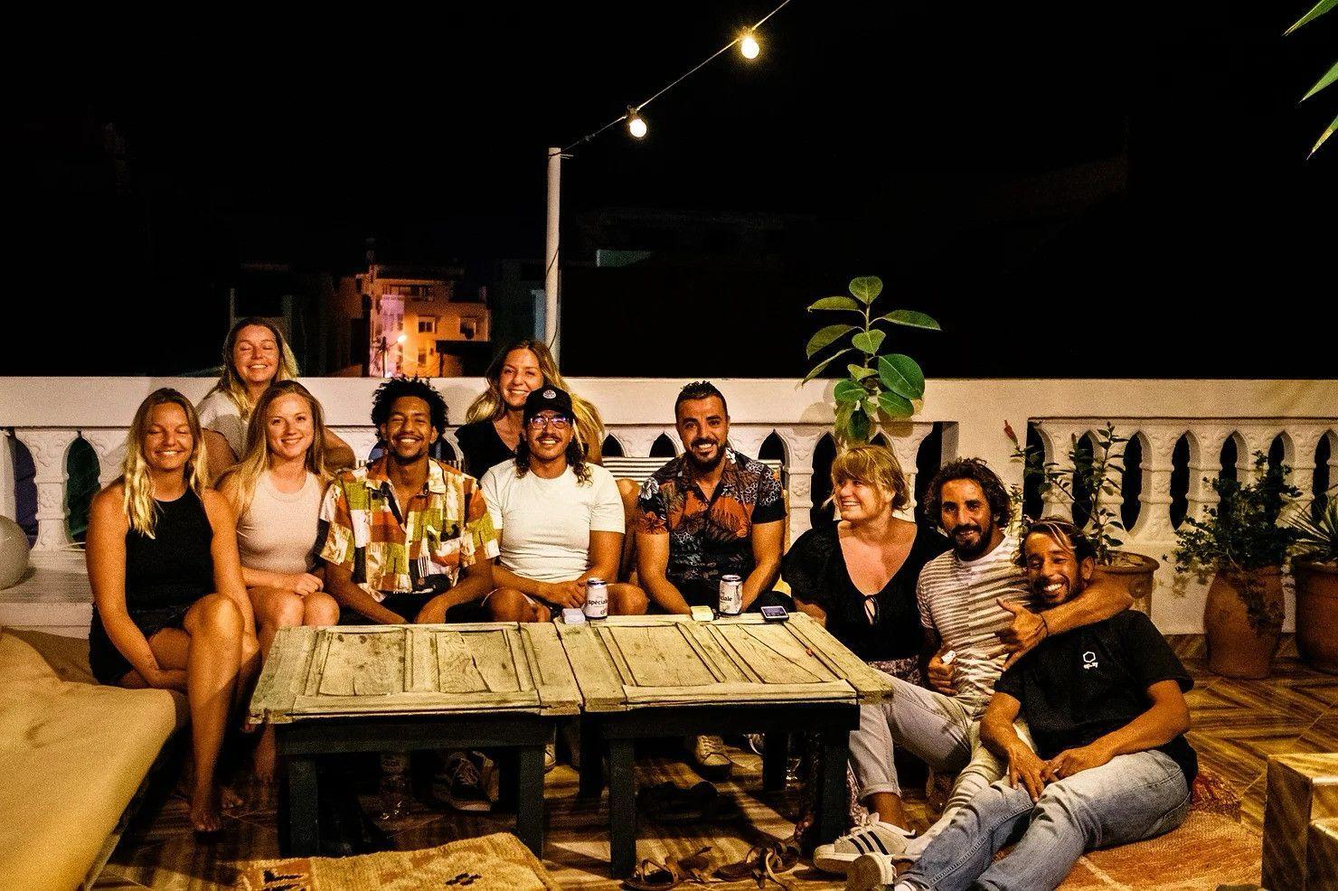Group of nomads gathered on the rooftop terrace at night with string lights
