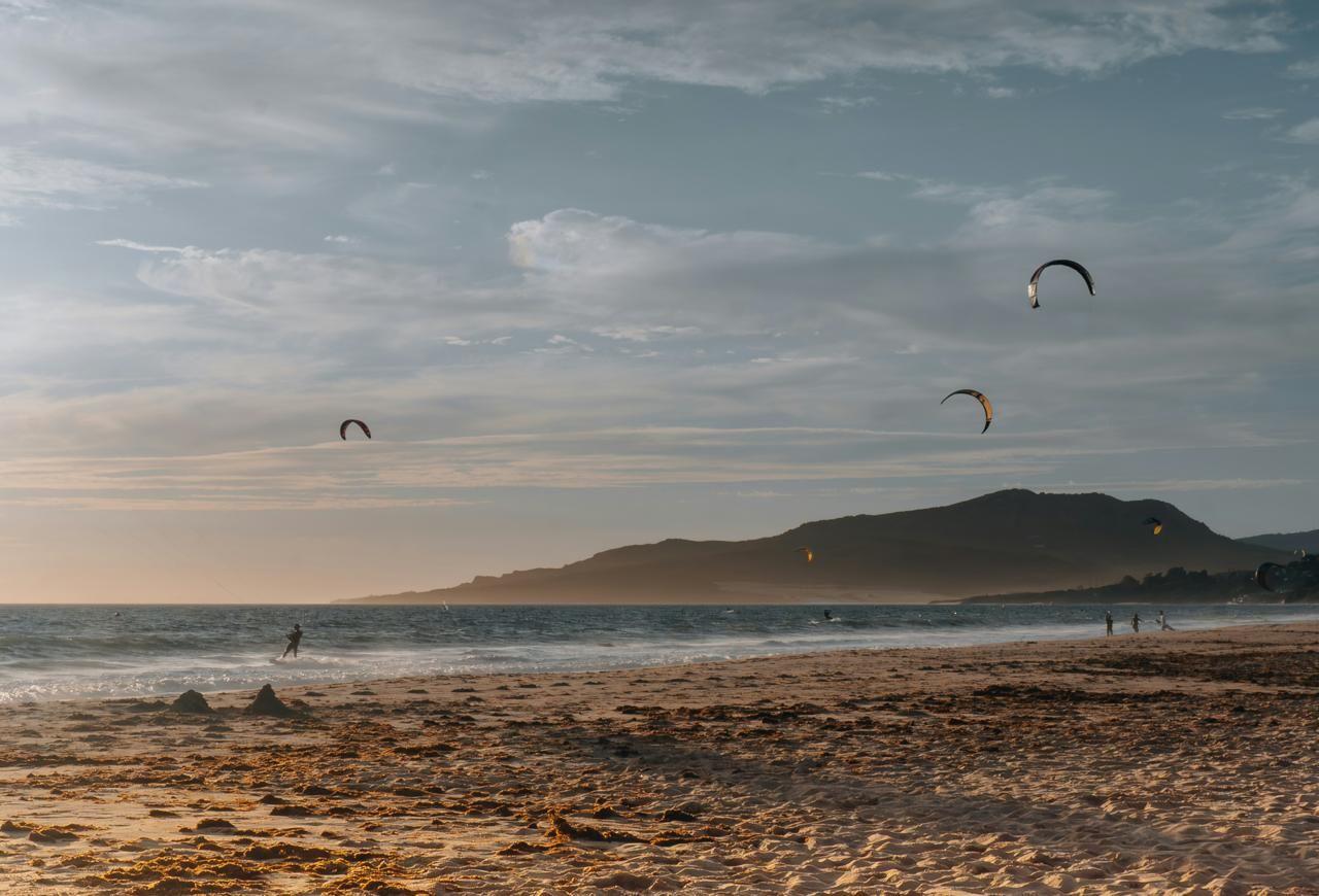 Tarifa beach at golden hour with kitesurfers in the air and mountains in the background