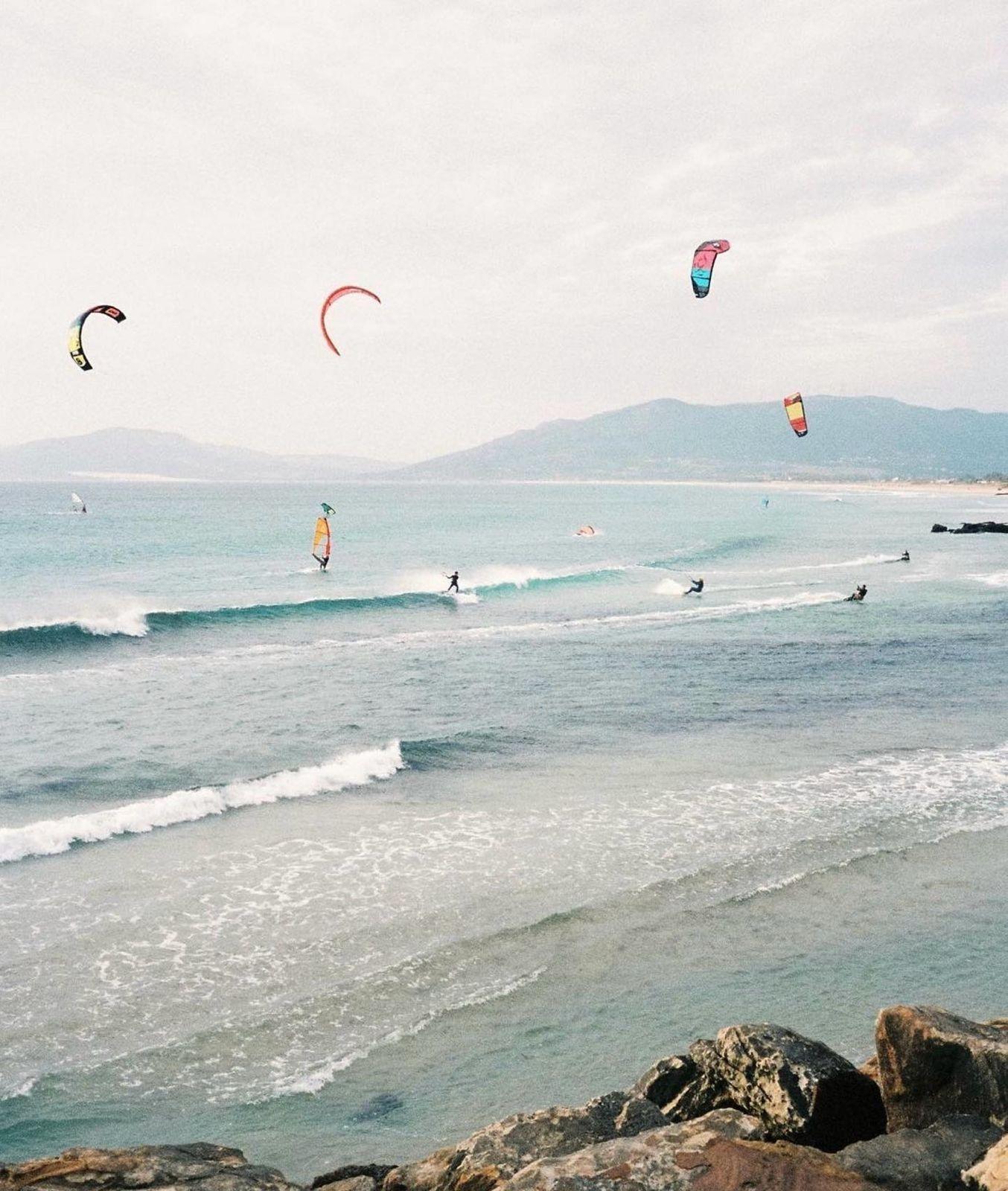 Multiple kitesurfers and windsurfers on the water at Tarifa with colorful kites in the sky