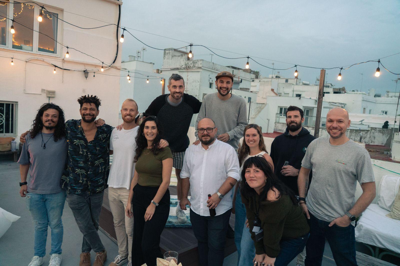 Group of coliving community members gathered on the rooftop terrace in Tarifa at dusk with string lights