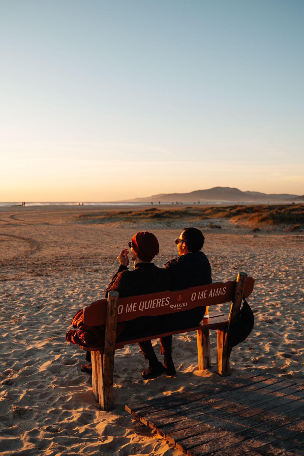 Two people sitting on a bench on the beach at Tarifa watching the sunset