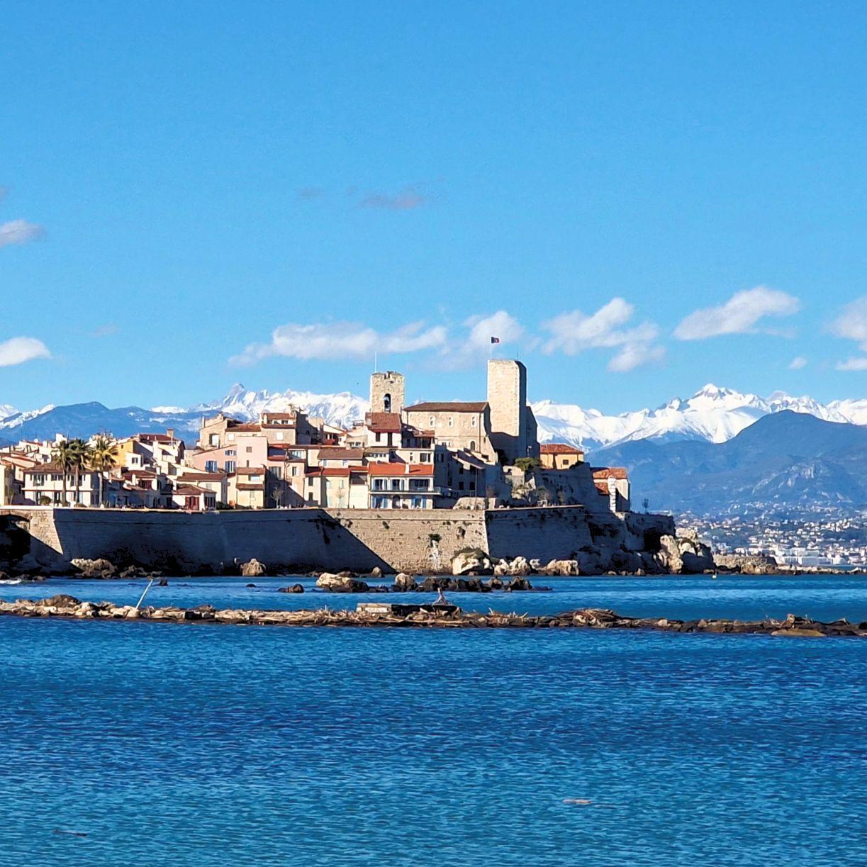 View of Antibes old town with snow-capped Alps in the background and turquoise Mediterranean sea